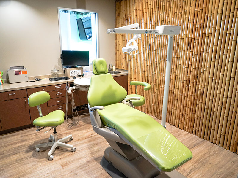 Treatment room with a green dental chair and bamboo wall